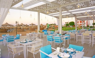 A restaurant with outdoor seating overlooking a beach. Tables are arranged under a canopy with hanging lights.