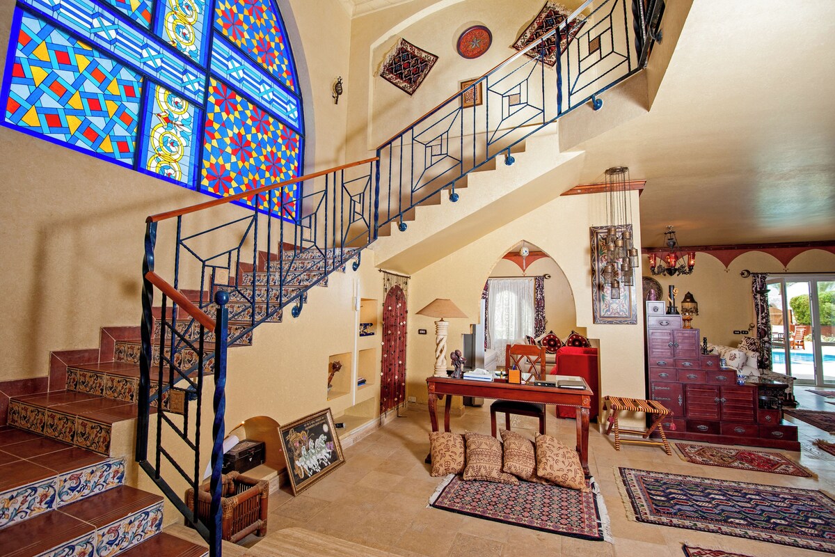 A spacious interior with a grand staircase, a large stained glass window, and a cozy seating area with a fireplace.