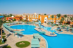 A large outdoor swimming pool with multiple lanes, surrounded by lounge chairs and umbrellas, and a building with traditional architecture in the background. - SUNRISE Garden Beach Resort - All inclusive (Hurghada)