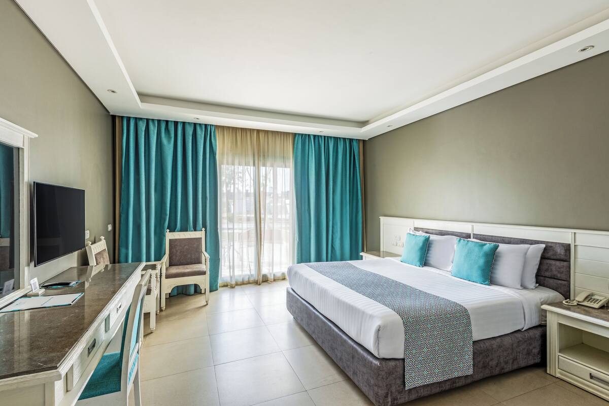 Una habitación de hotel con cama, escritorio, computadora, silla y televisor.