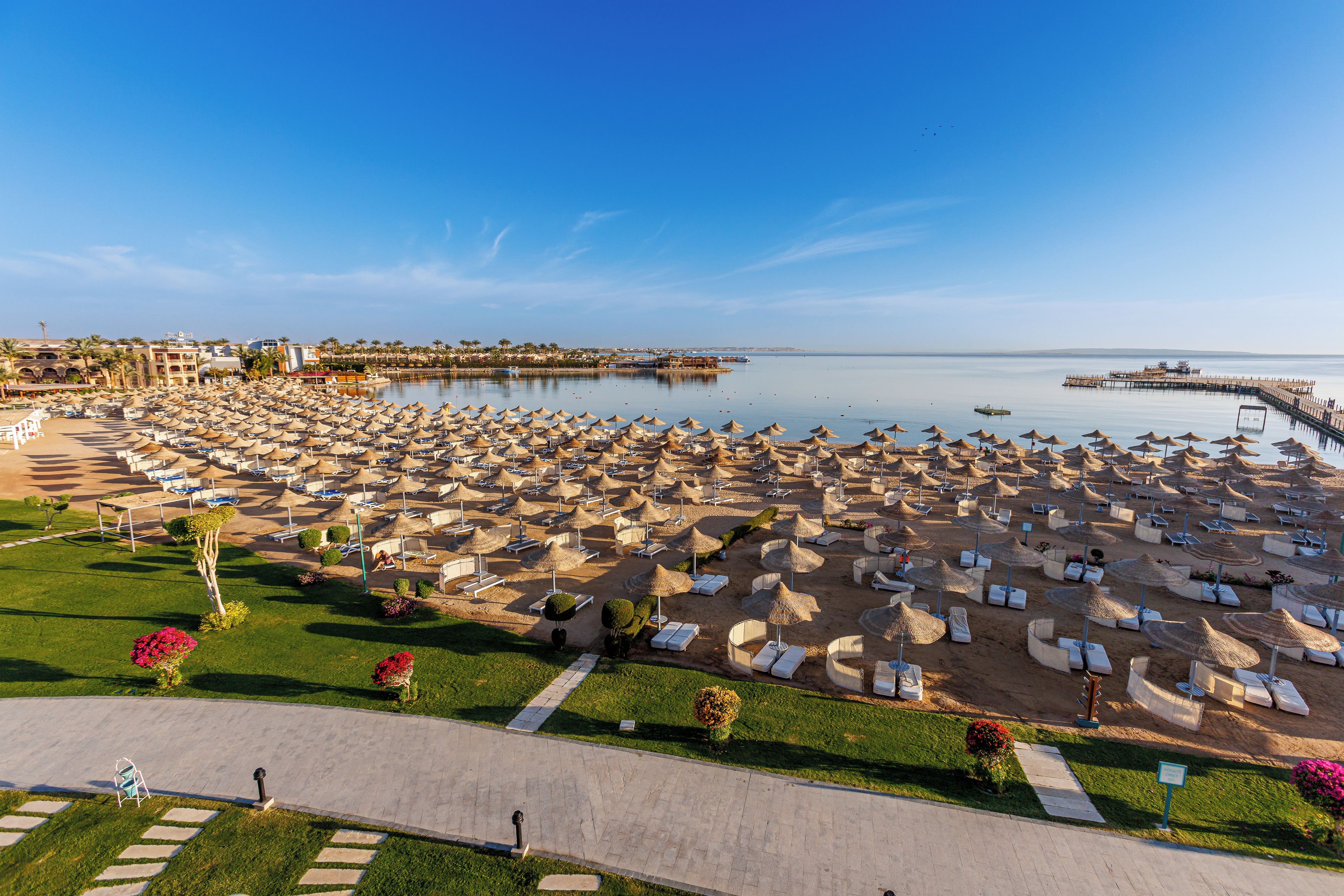 Een strandresort met tal van ligbedden en parasols, een heldere lucht en een kalme zee.
