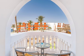 A balcony with a glass table and chairs, overlooking a building with orange and white architecture, palm trees, and a clear sky. - SUNRISE Garden Beach Resort - All inclusive (Hurghada)