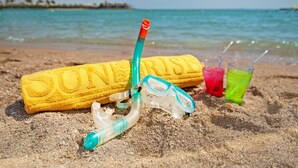 Ein Strandbild mit Sandburg, Schnorchelausrüstung und Getränken im Sand.