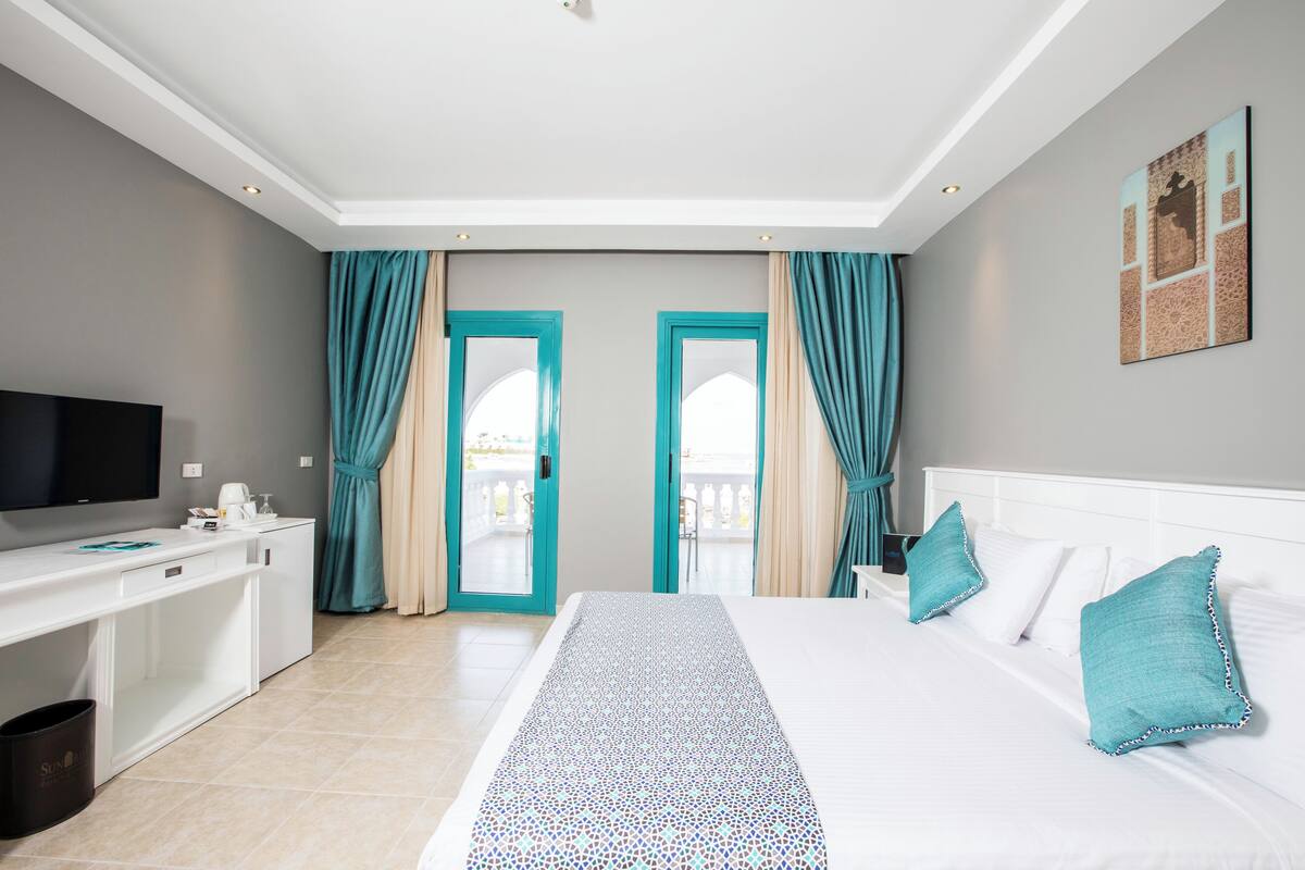 Una habitación de hotel con cama, televisor, escritorio y vistas al balcón.