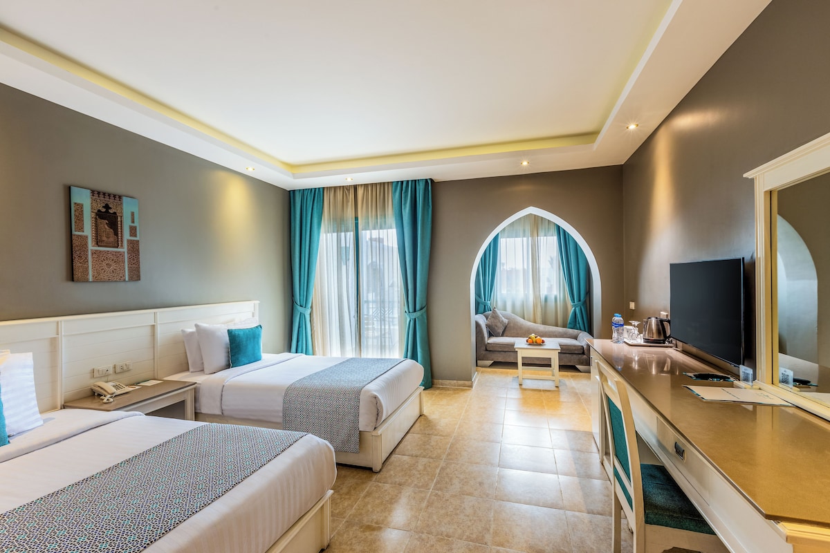 A hotel room with two beds, a sofa, a TV, and a coffee maker.