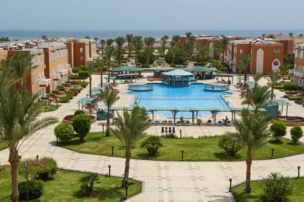 A resort with a central swimming pool, palm trees, and a view of the sea.