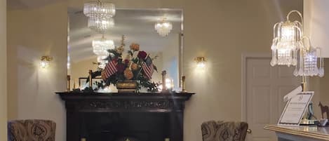 A room with a fireplace, two patterned armchairs, a mirror, and multiple chandeliers.