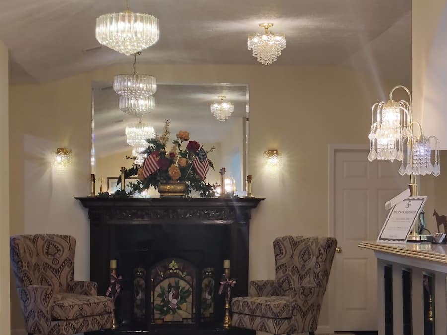 Una habitación con chimenea, dos sillones estampados, un espejo y varios candelabros.