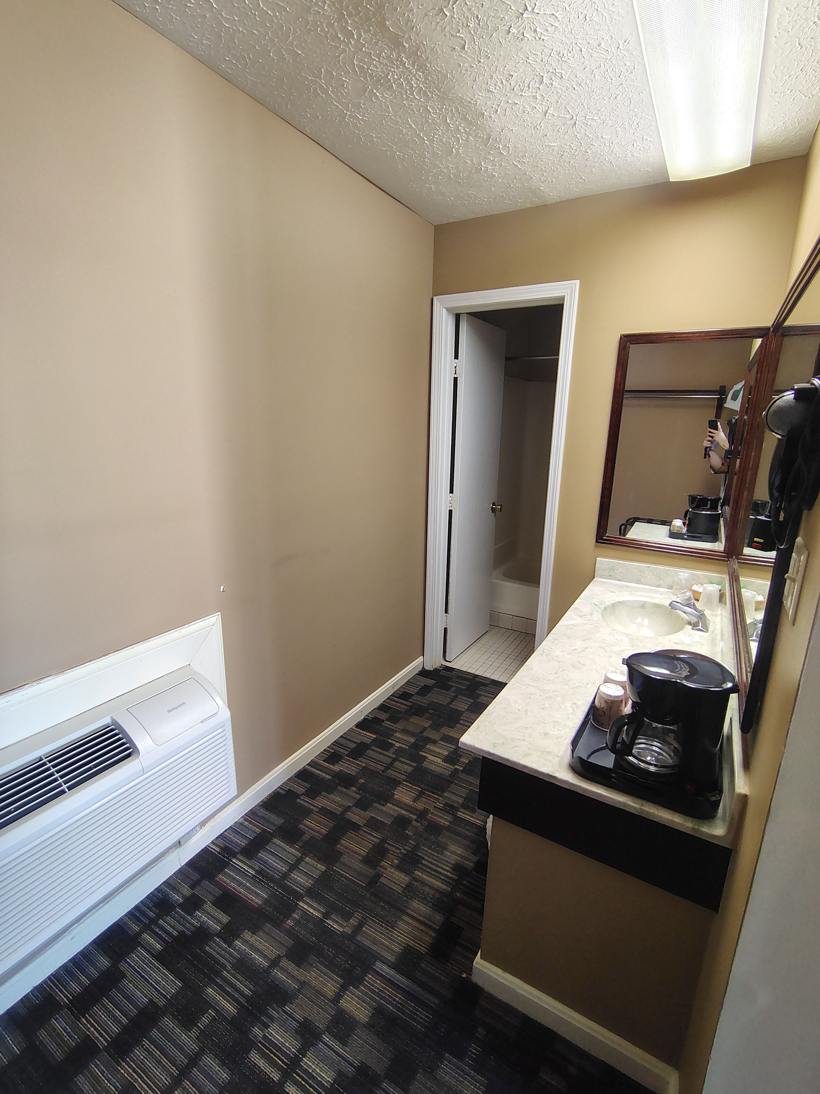 A small bathroom with a white air conditioner, a sink with a mirror, and a patterned floor.