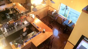 A bar area with a counter, stools, and a large mirror. There are tables and chairs in the dining area, and a window with a view.