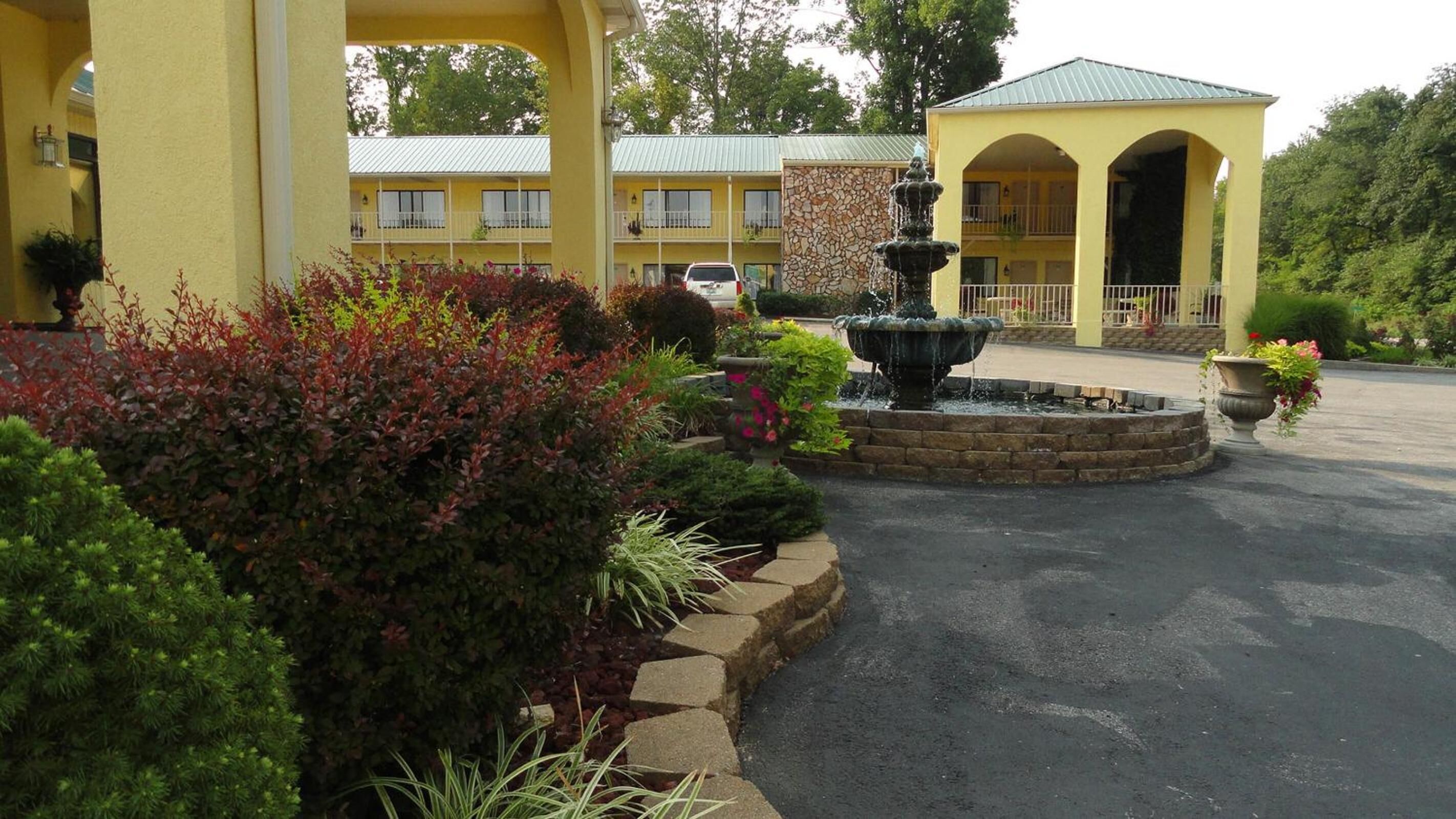 A yellow building with a fountain, surrounded by landscaped gardens and a parking lot.