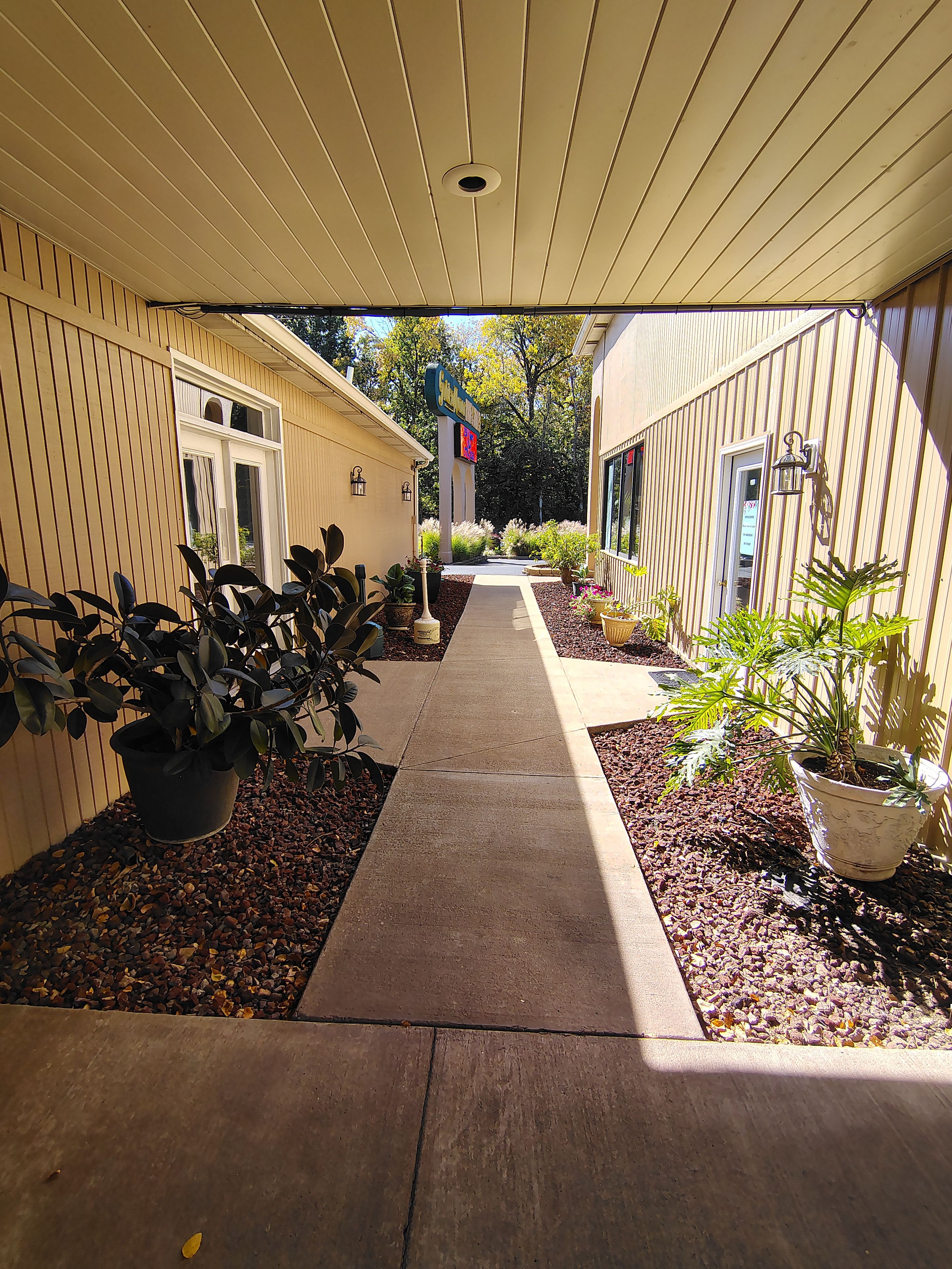 A covered walkway with potted plants and a signboard.