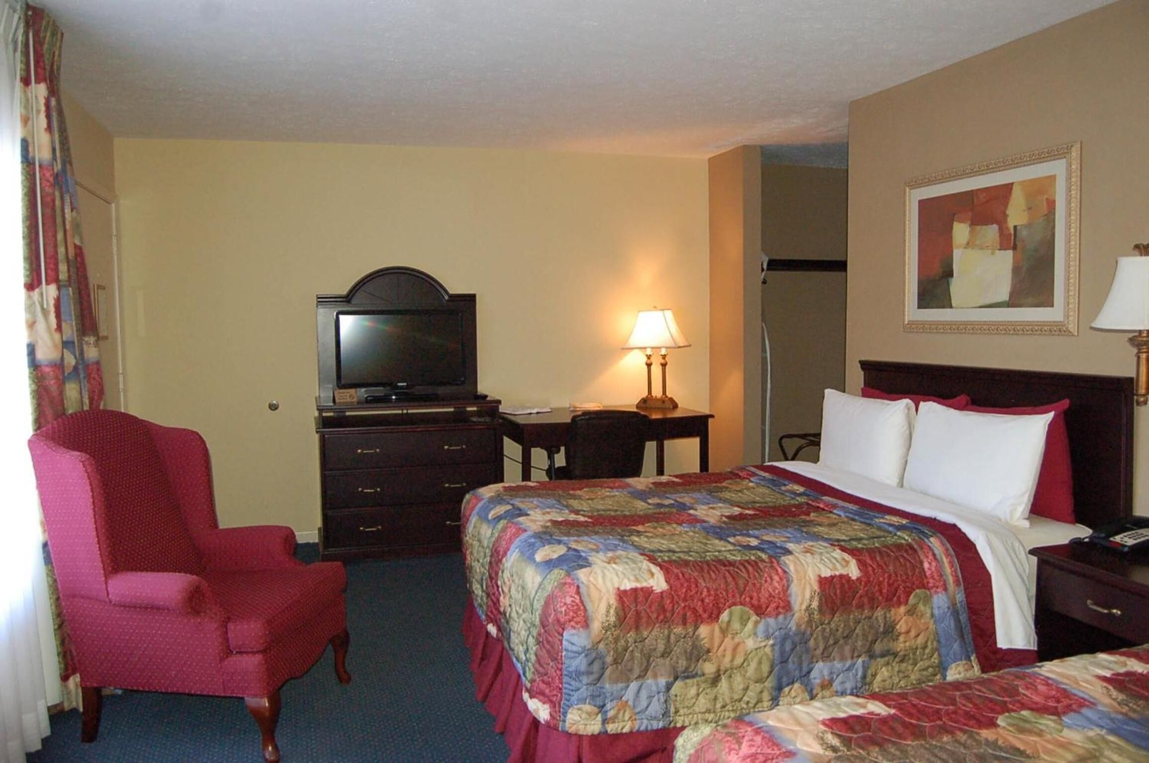 Quarto de hotel com cama, cadeira, escrivaninha, televisão e abajur.