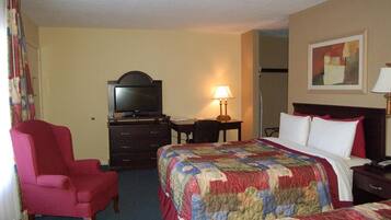 Quarto de hotel com cama, cadeira, escrivaninha, televisão e abajur.