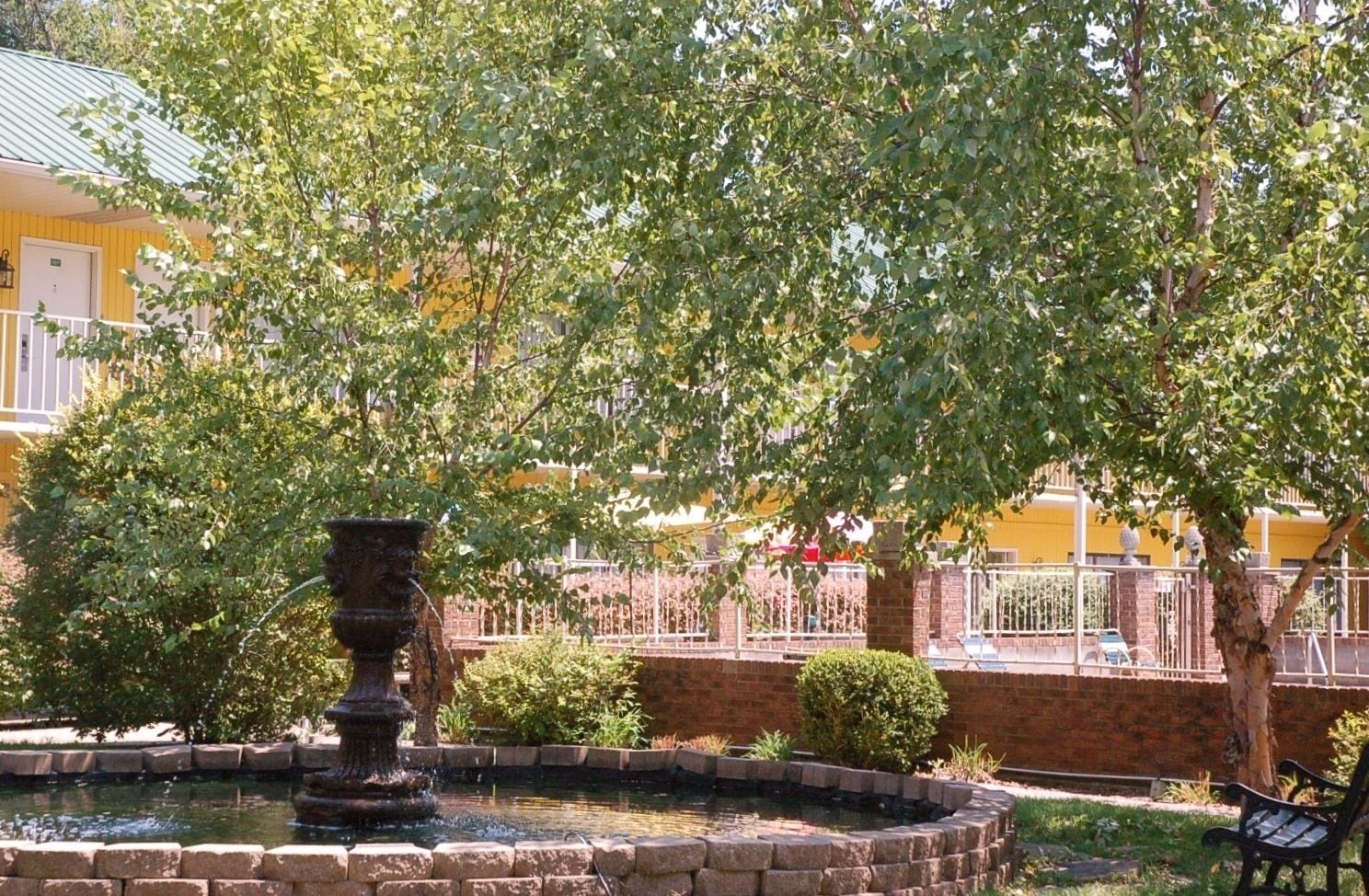 A fountain surrounded by a brick border, with a yellow building in the background.