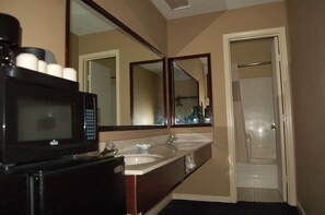 A bathroom with a double sink, a mirror, a microwave, and a shower. - Golden Manor Inn & Suites (Muldraugh)