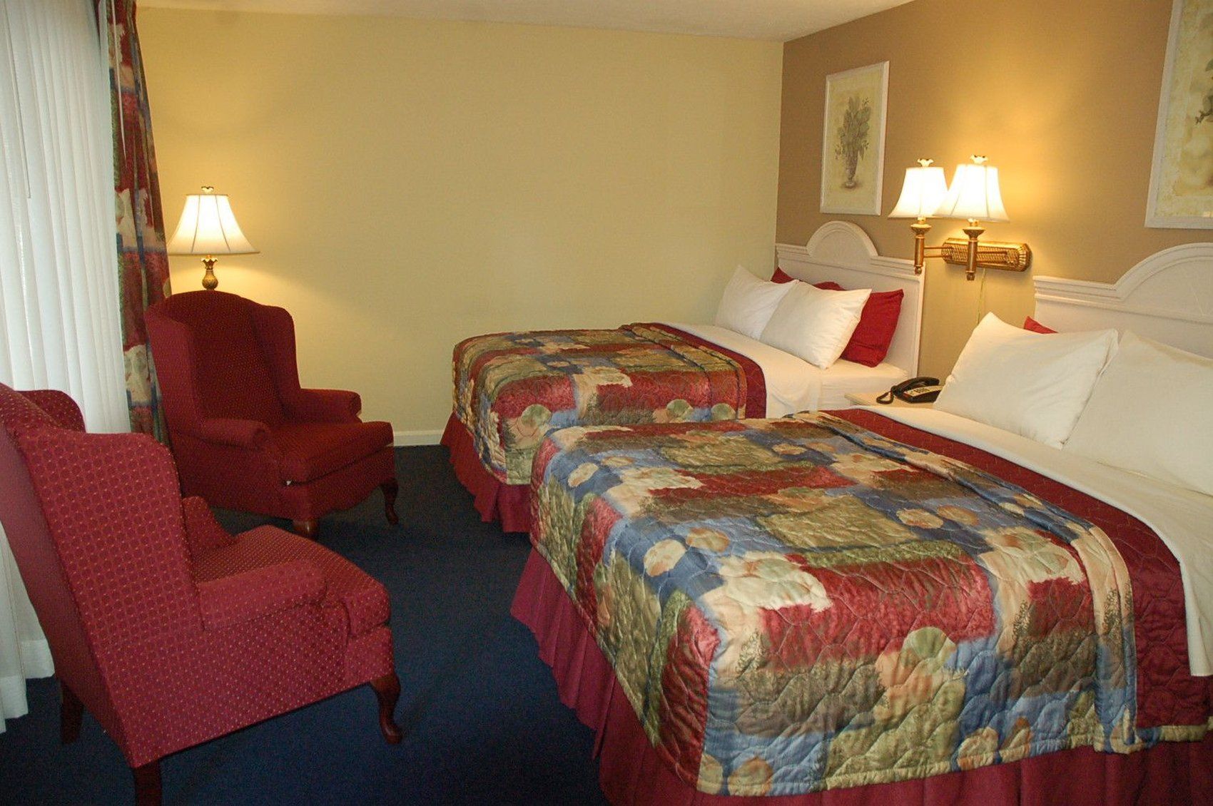 A hotel room with two beds, a red armchair, and two bedside lamps.