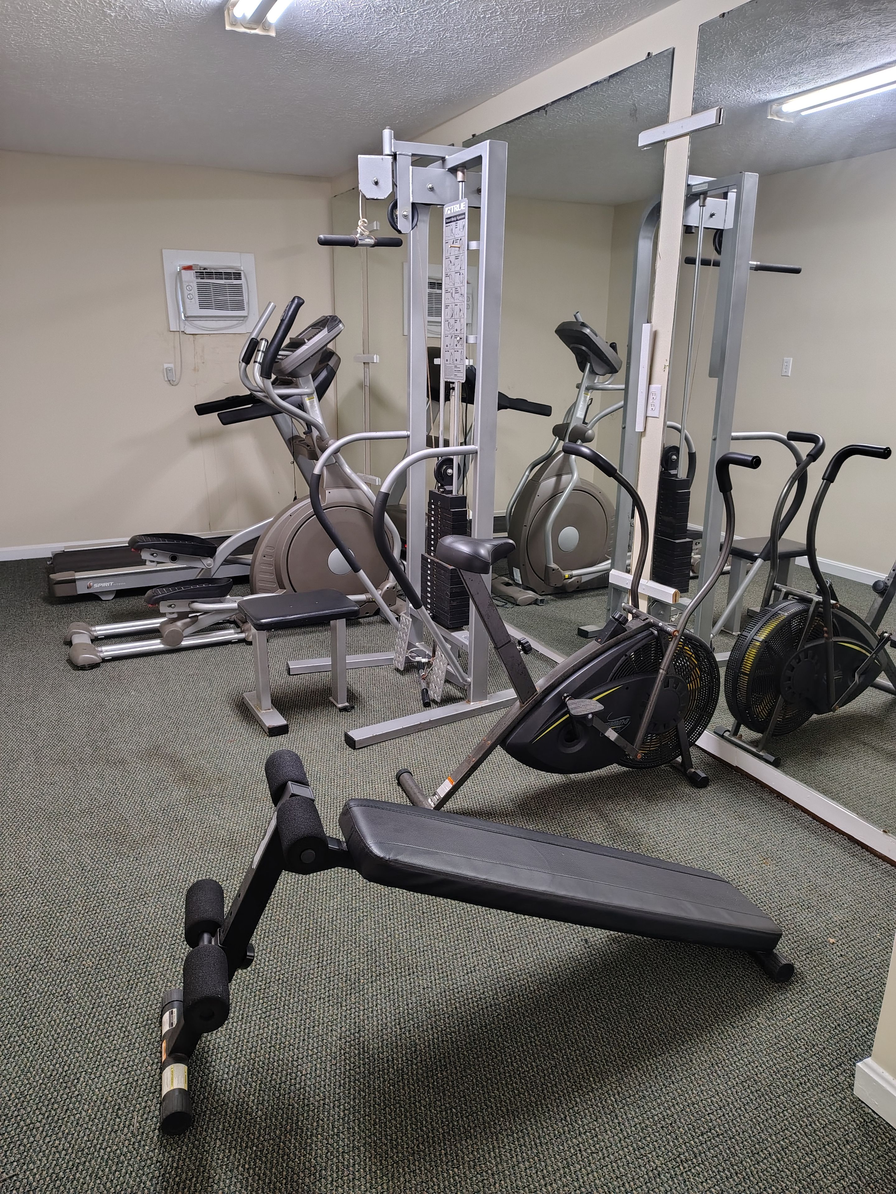 Un gimnasio con equipo de ejercicio, incluyendo una cinta de correr, una elíptica y máquinas de pesas.