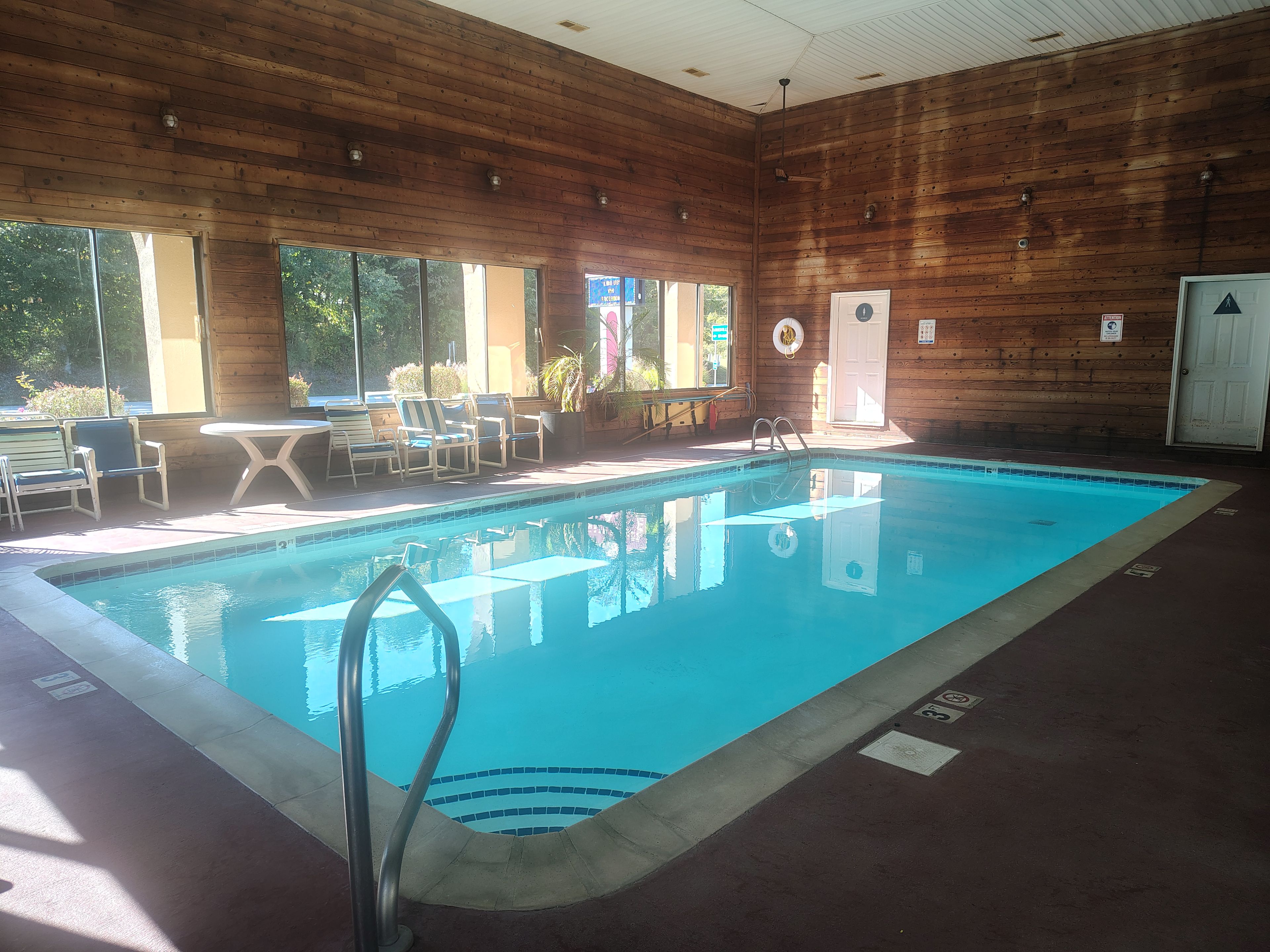 A swimming pool with a wooden deck, lounge chairs, and a view of the outdoors.