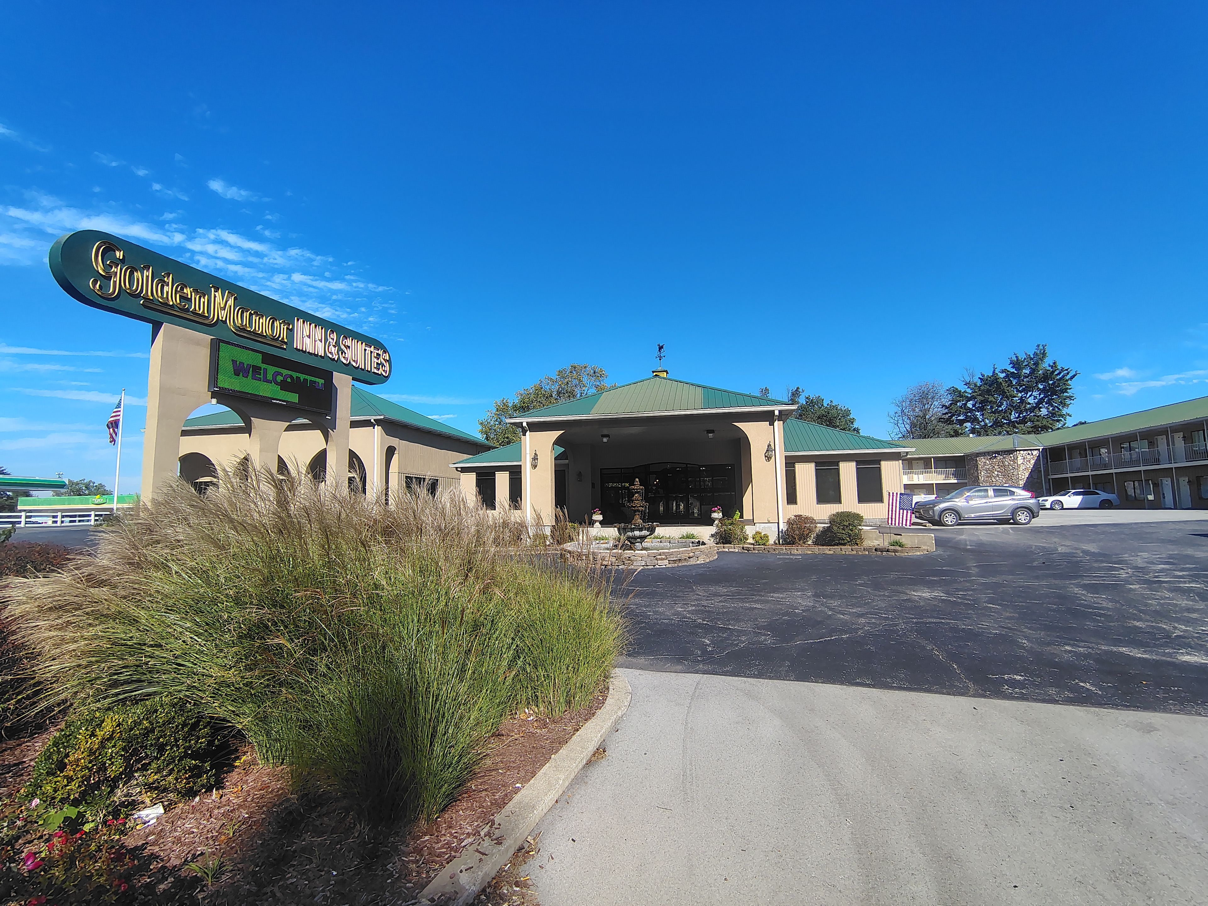 A hotel entrance with a sign, a covered parking area, and a building with a green roof.