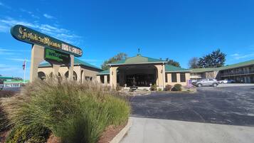 A hotel entrance with a sign, a covered parking area, and a building with a green roof.