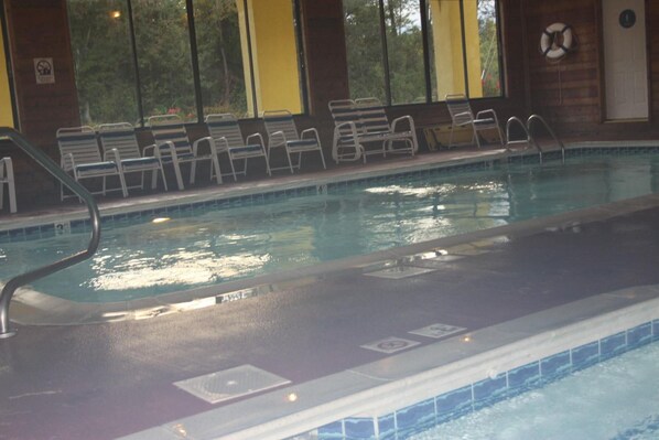 An indoor swimming pool with clear water, metal pool ladders, and a row of empty chairs along the edge. - Golden Manor Inn & Suites (Muldraugh)