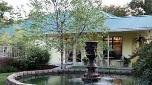 A fountain in a circular stone basin, surrounded by a brick border, with a building in the background.