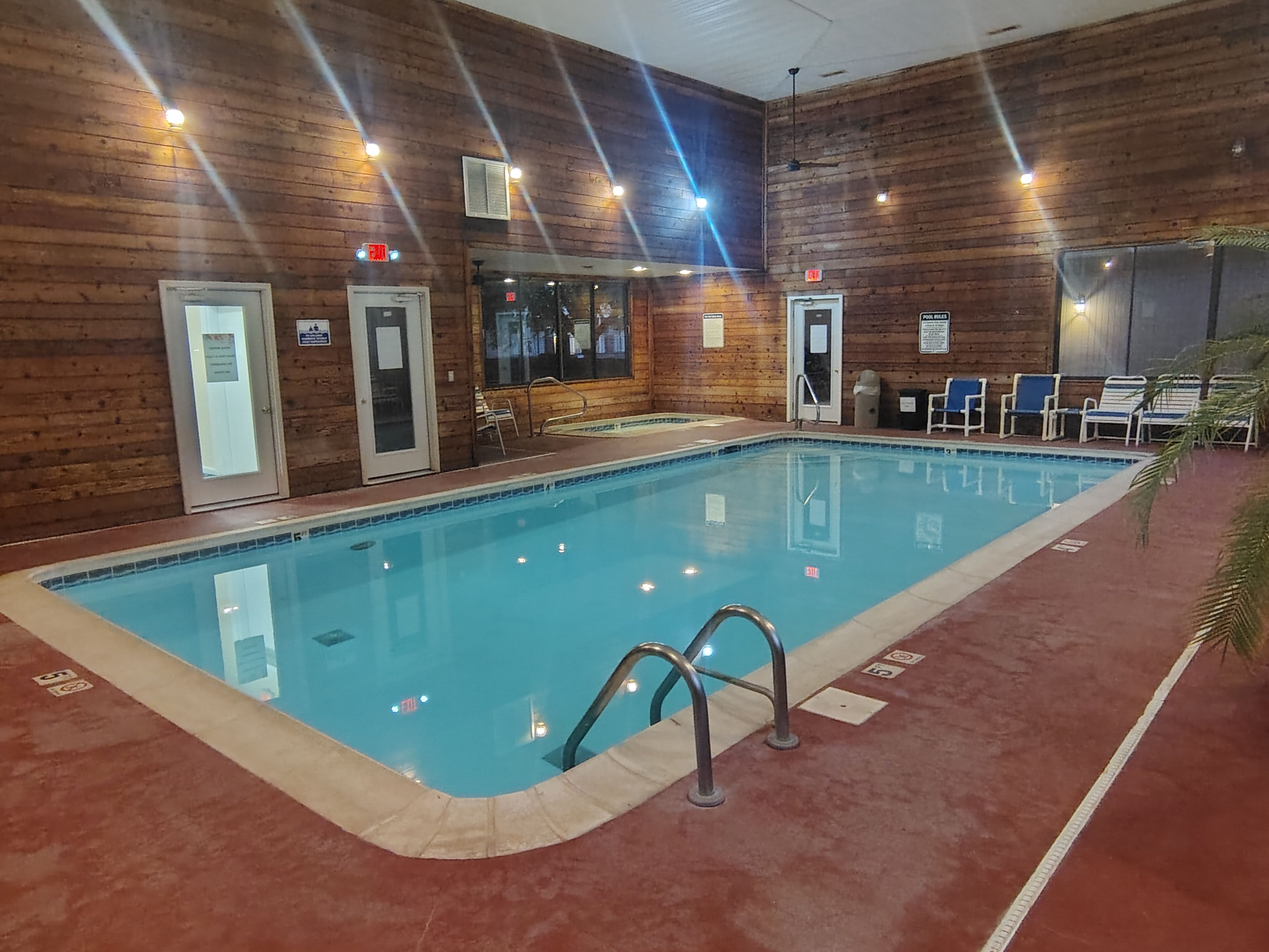 An indoor swimming pool with wooden walls, a tiled floor, and a few lounge chairs.