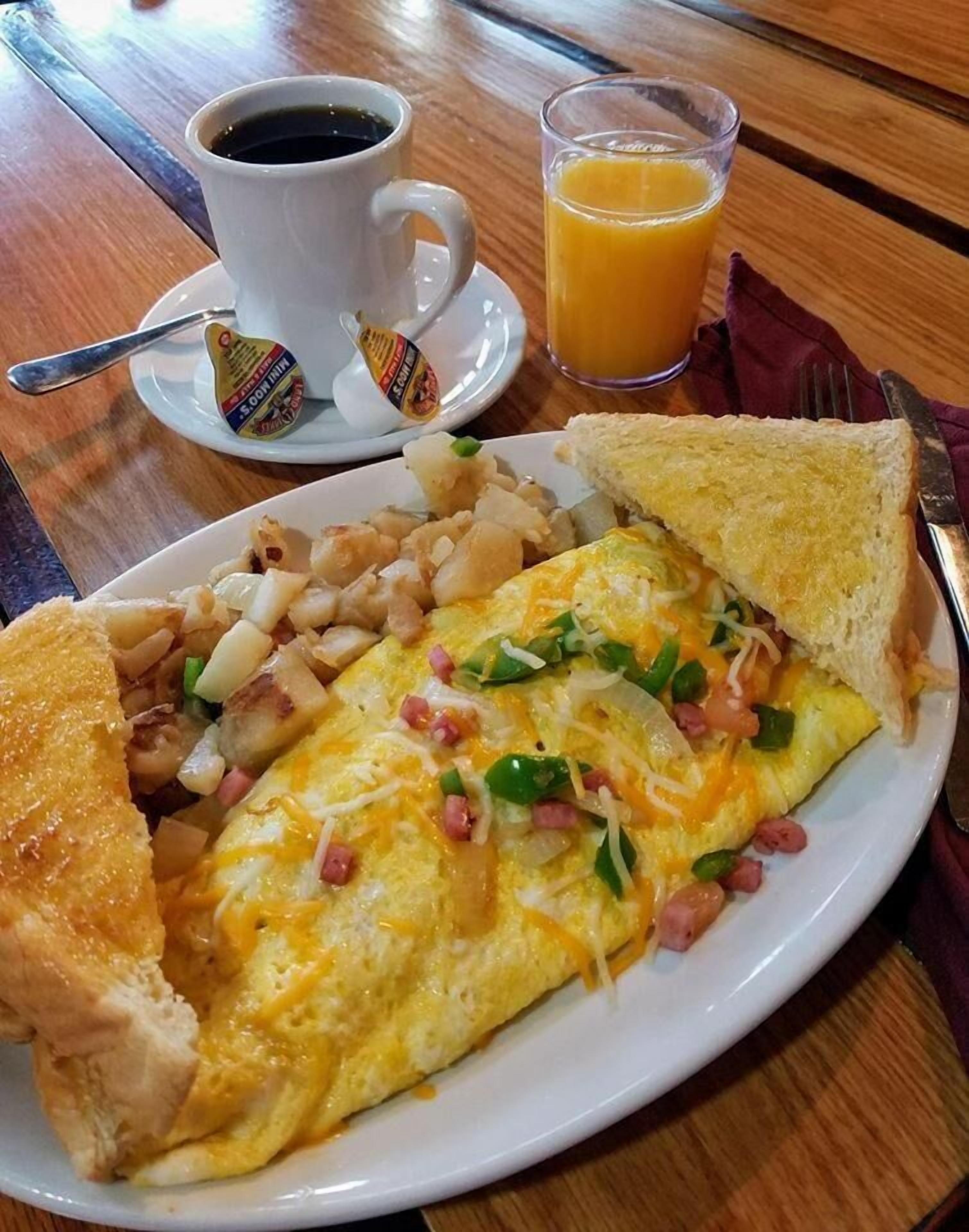 Un plato de desayuno con huevos, jamón, queso y tostadas, acompañado de una taza de café y un vaso de jugo de naranja.