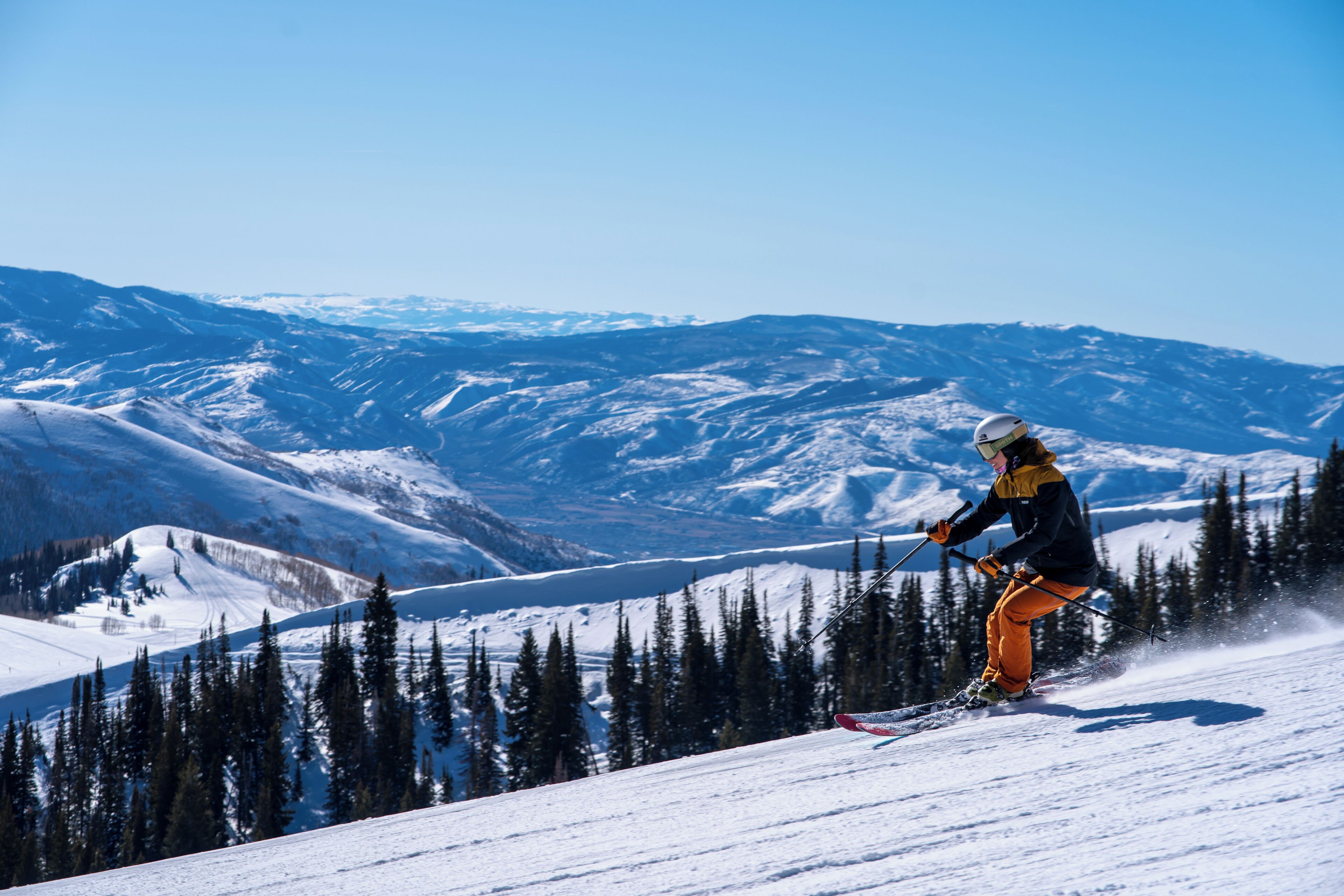 A person skiing on a snowy mountain slope with a clear sky and distant mountains.