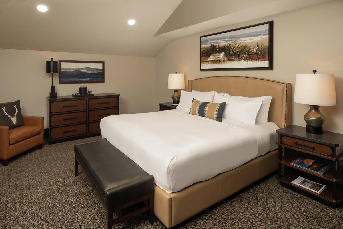 A hotel room with a large bed, a brown leather sofa, a small table with a lamp, a dresser, and a painting on the wall.