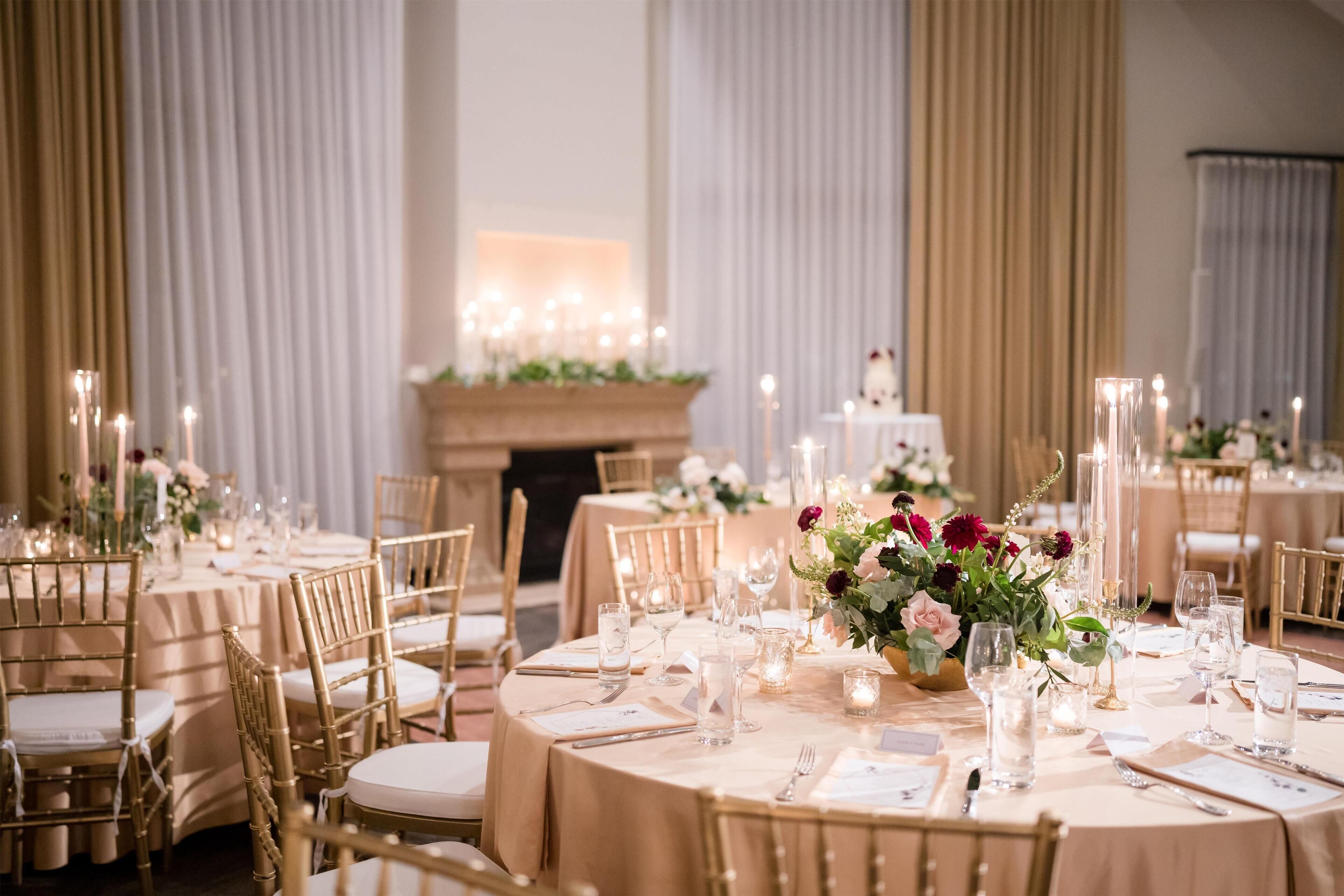 Un salón de banquetes con mesas redondas dispuestas para un evento formal, con sillas doradas, manteles blancos y centros de mesa florales.