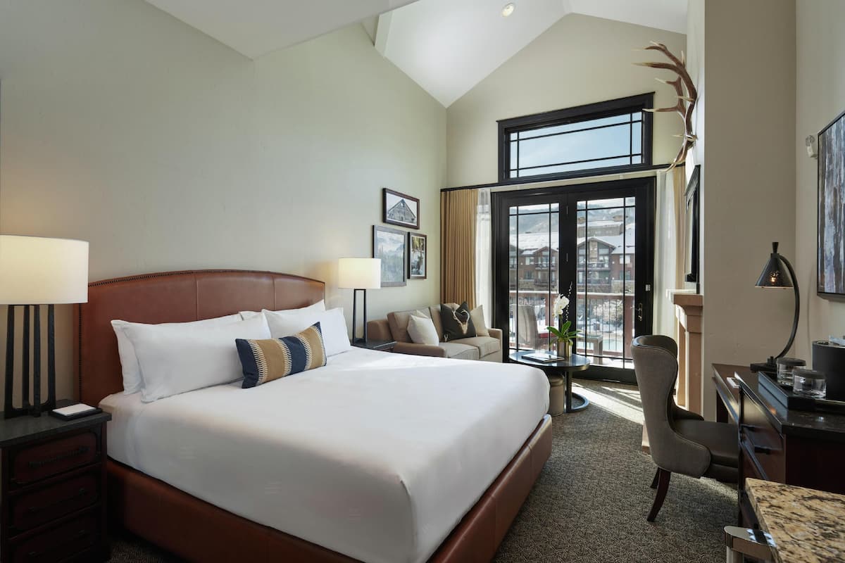 A hotel room with a large bed, a desk, a chair, and a view of the outside.