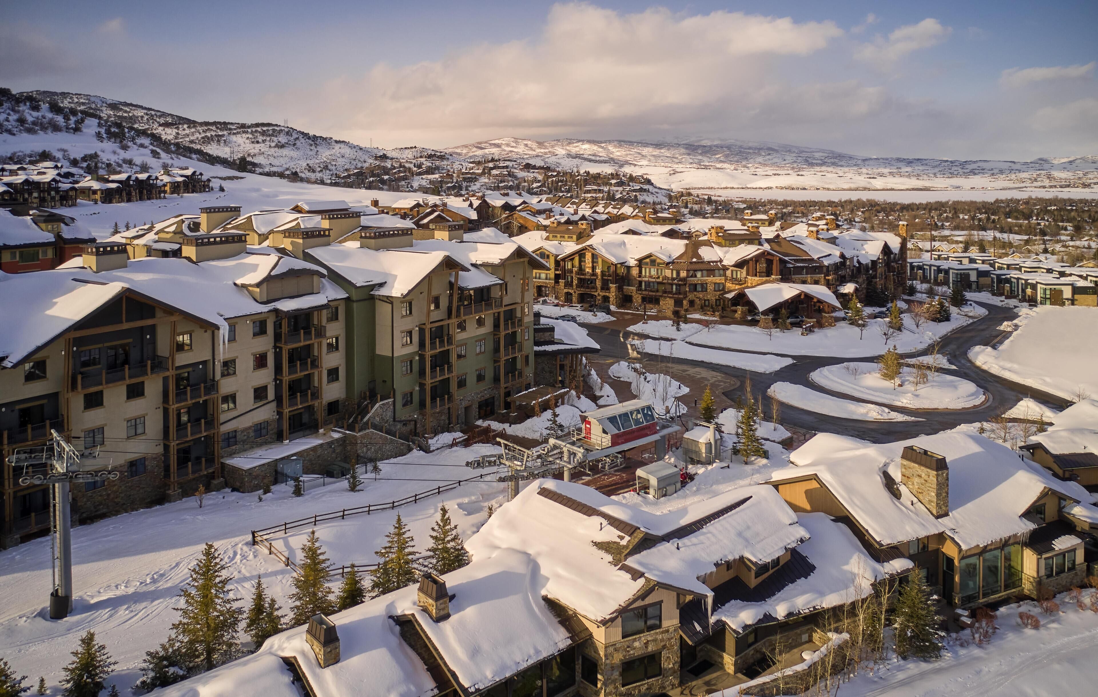 A snow-covered resort with multiple buildings, a ski lift, and a winding road.