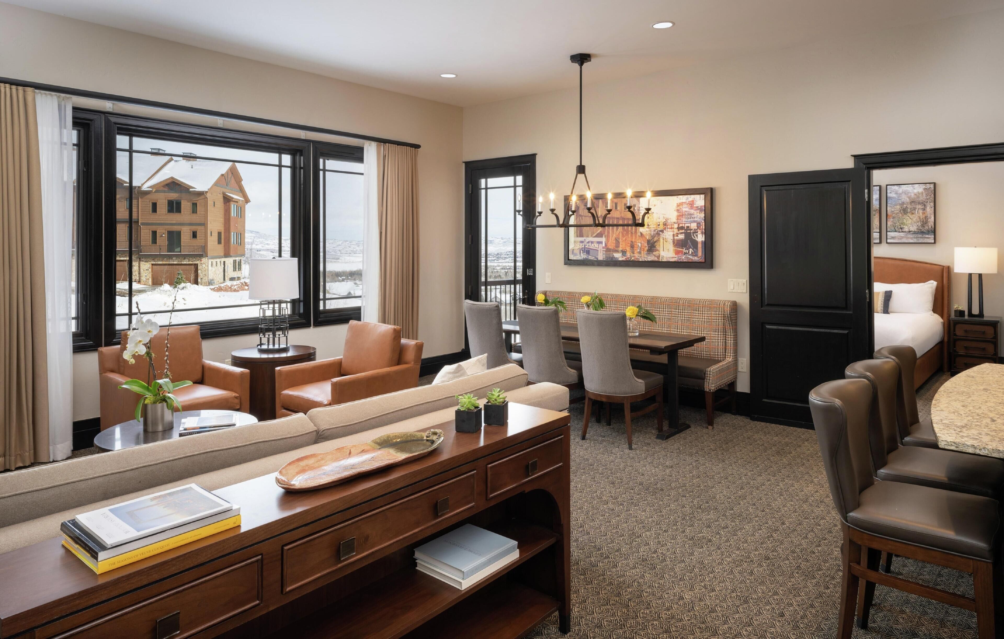 A hotel room with a large window, a sofa, a dining table, and a bed.
