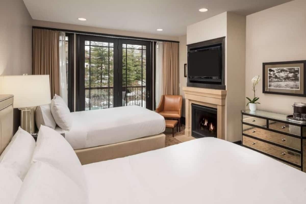 A hotel room with two beds, a fireplace, a TV, and a large window with curtains.
