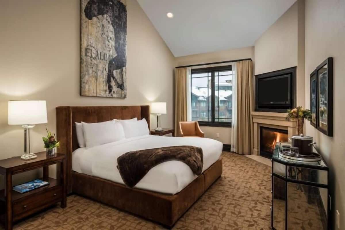 A hotel room with a large bed, a television, a fireplace, and a window with curtains.