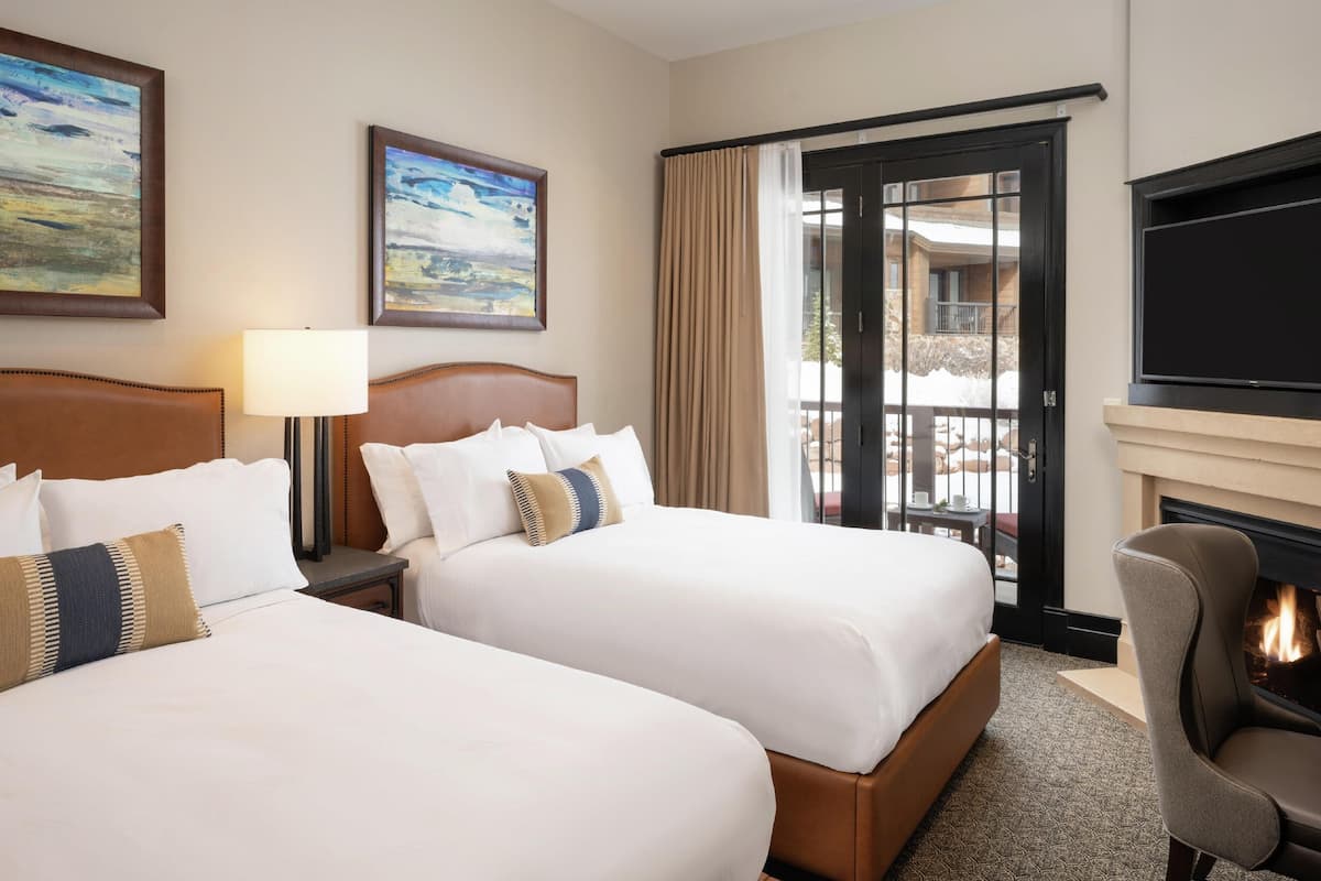 A hotel room with two beds, a TV, a fireplace, and a balcony with a view.