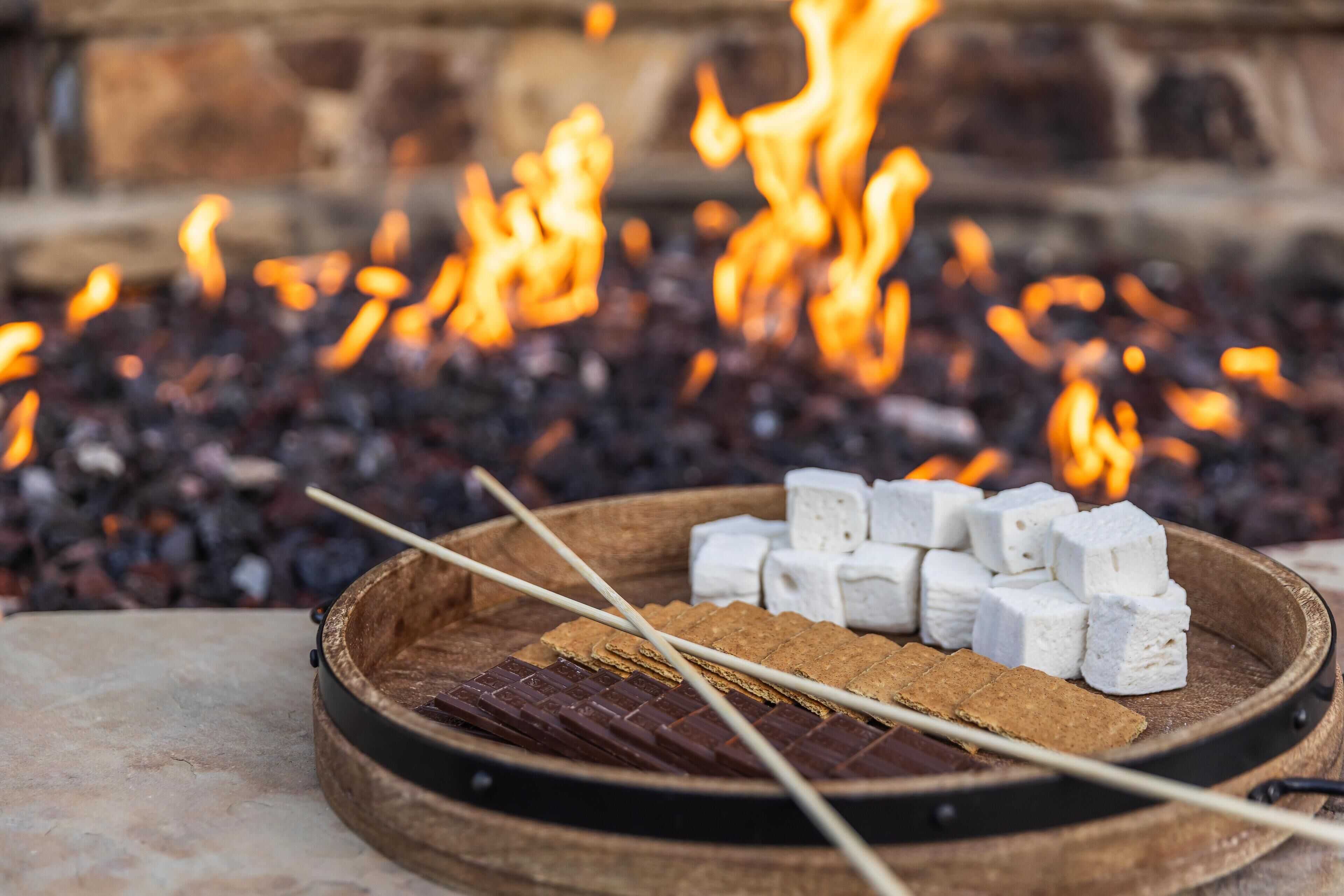 Un feu de camp avec des guimauves et du chocolat sur un plateau en bois.