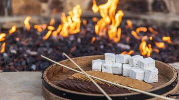 Un feu de camp avec des guimauves et du chocolat sur un plateau en bois.