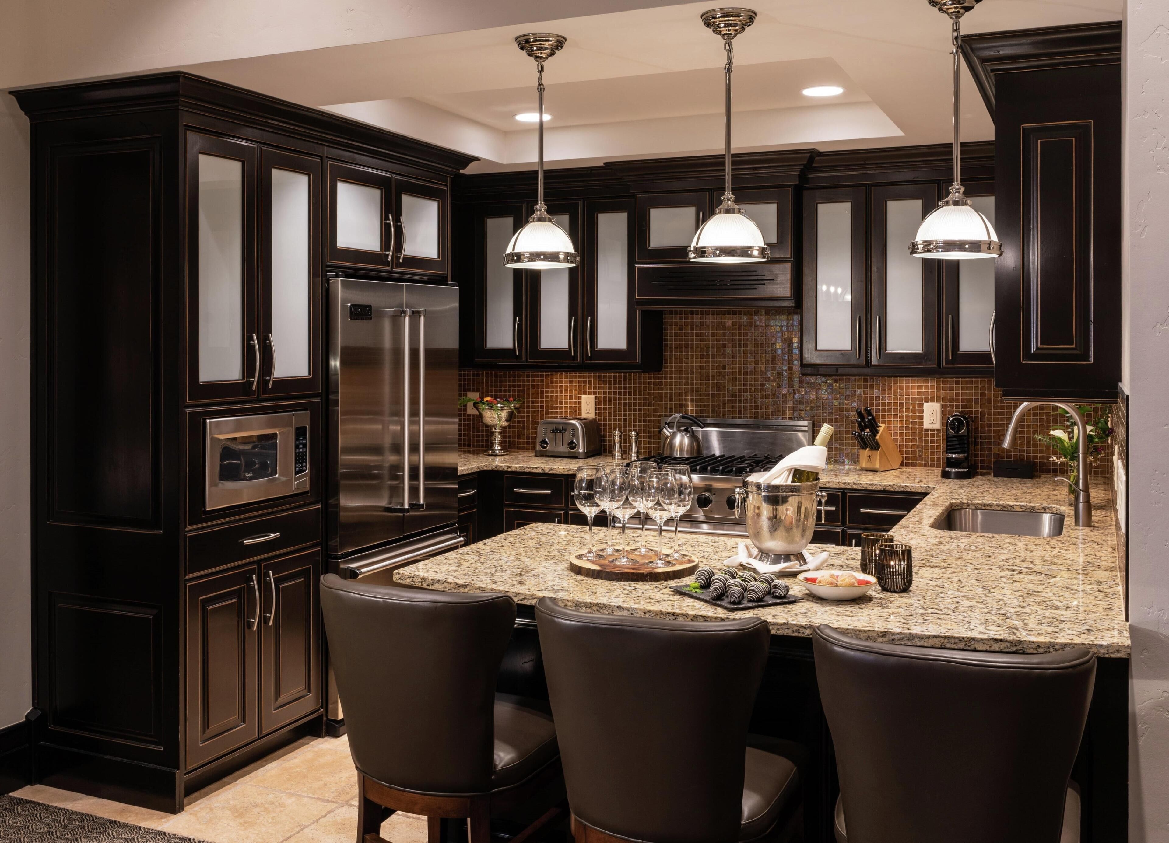 A modern kitchen with dark wood cabinets, stainless steel appliances, granite countertops, and pendant lighting.