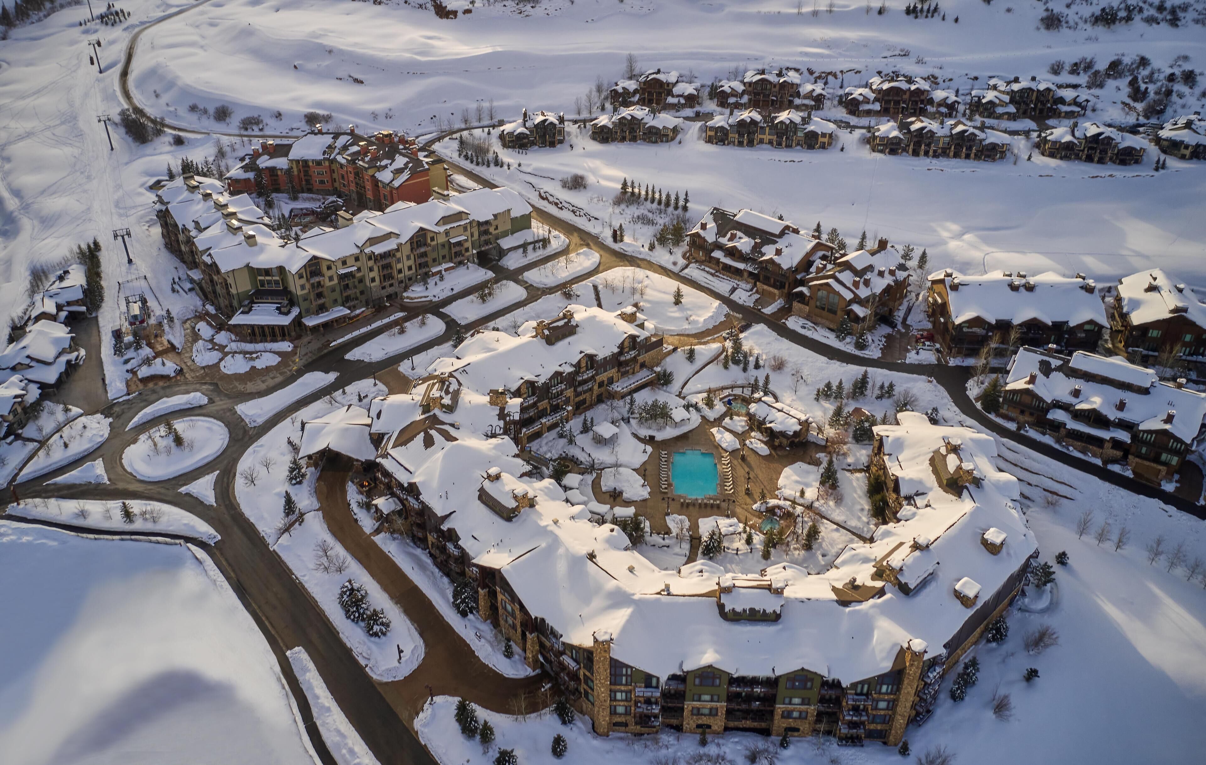 An aerial view of a snow-covered resort with multiple buildings, a central pool area, and interconnected roads.