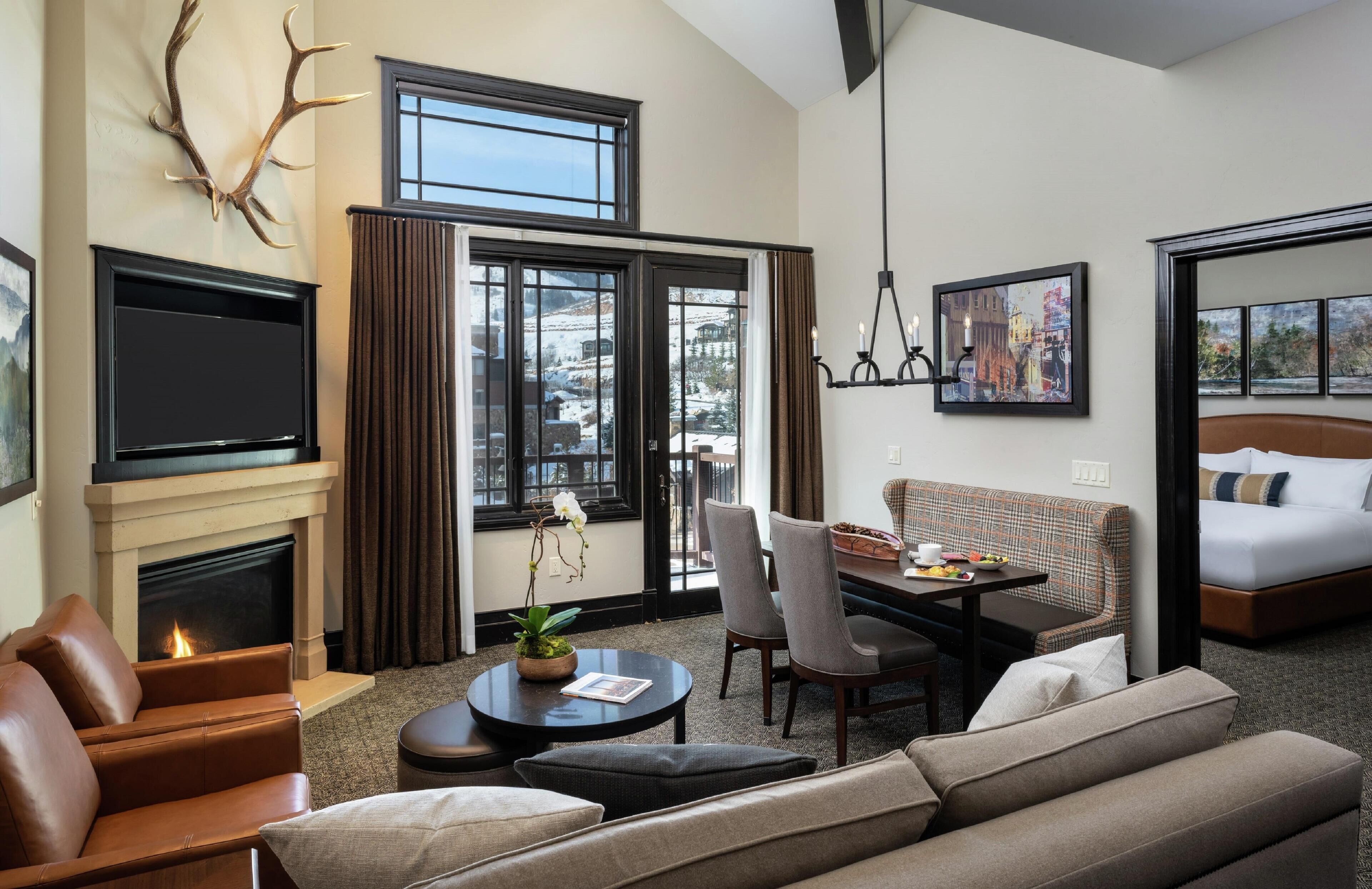A modern hotel room with a fireplace, a dining area, a sofa, and a bed.