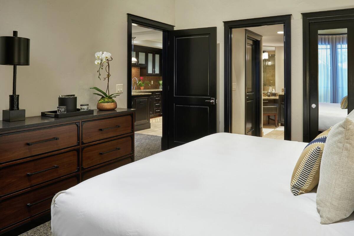 A hotel room with a bed, a dresser, a lamp, and a potted orchid.