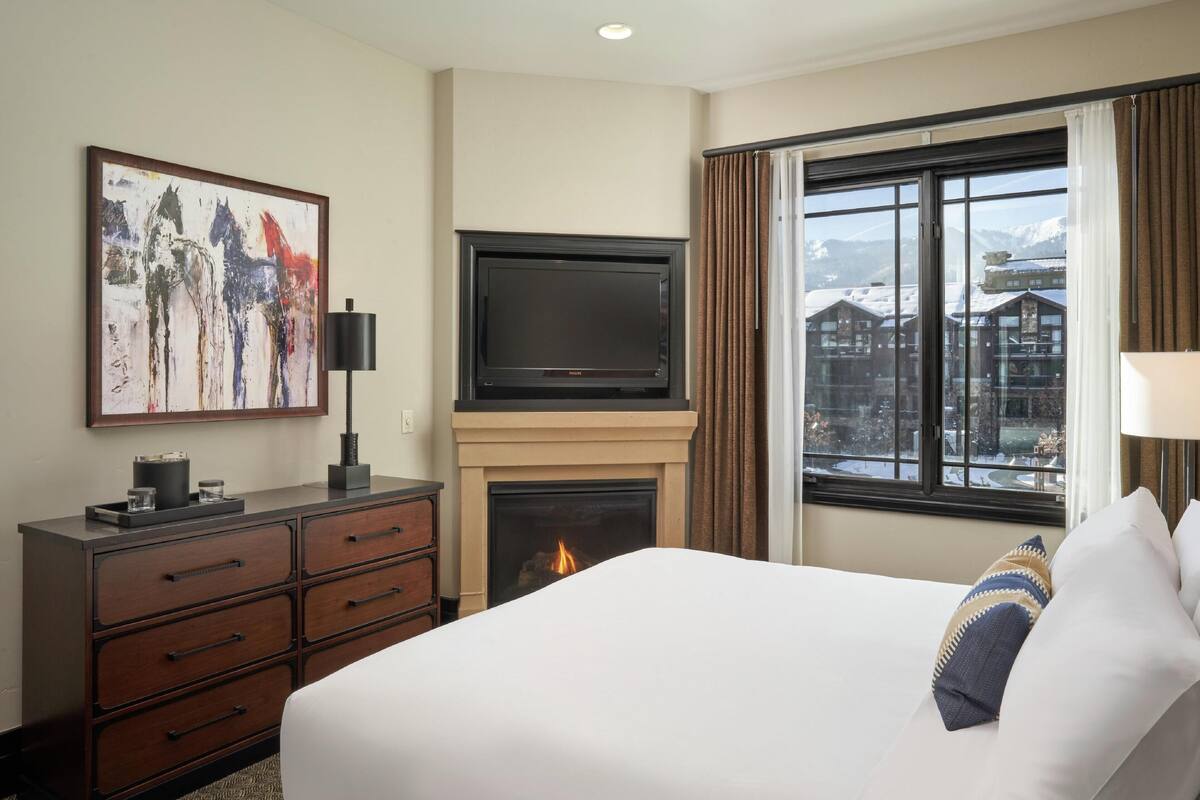 A hotel room with a bed, a fireplace, a TV, a dresser, and a painting.