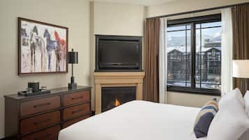 A hotel room with a bed, a fireplace, a TV, a dresser, and a painting.