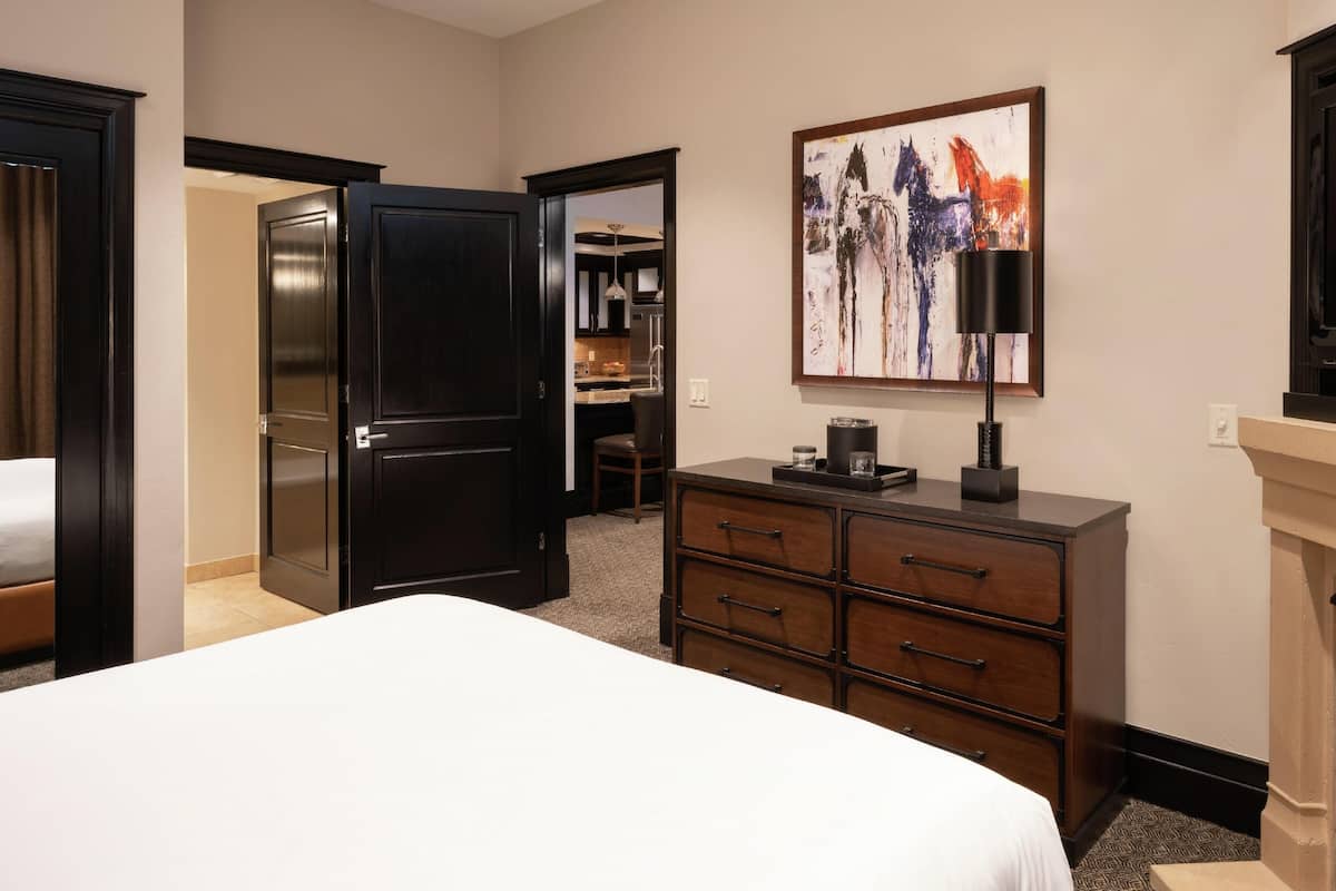 A hotel room with a bed, a dresser, a painting, and a fireplace.