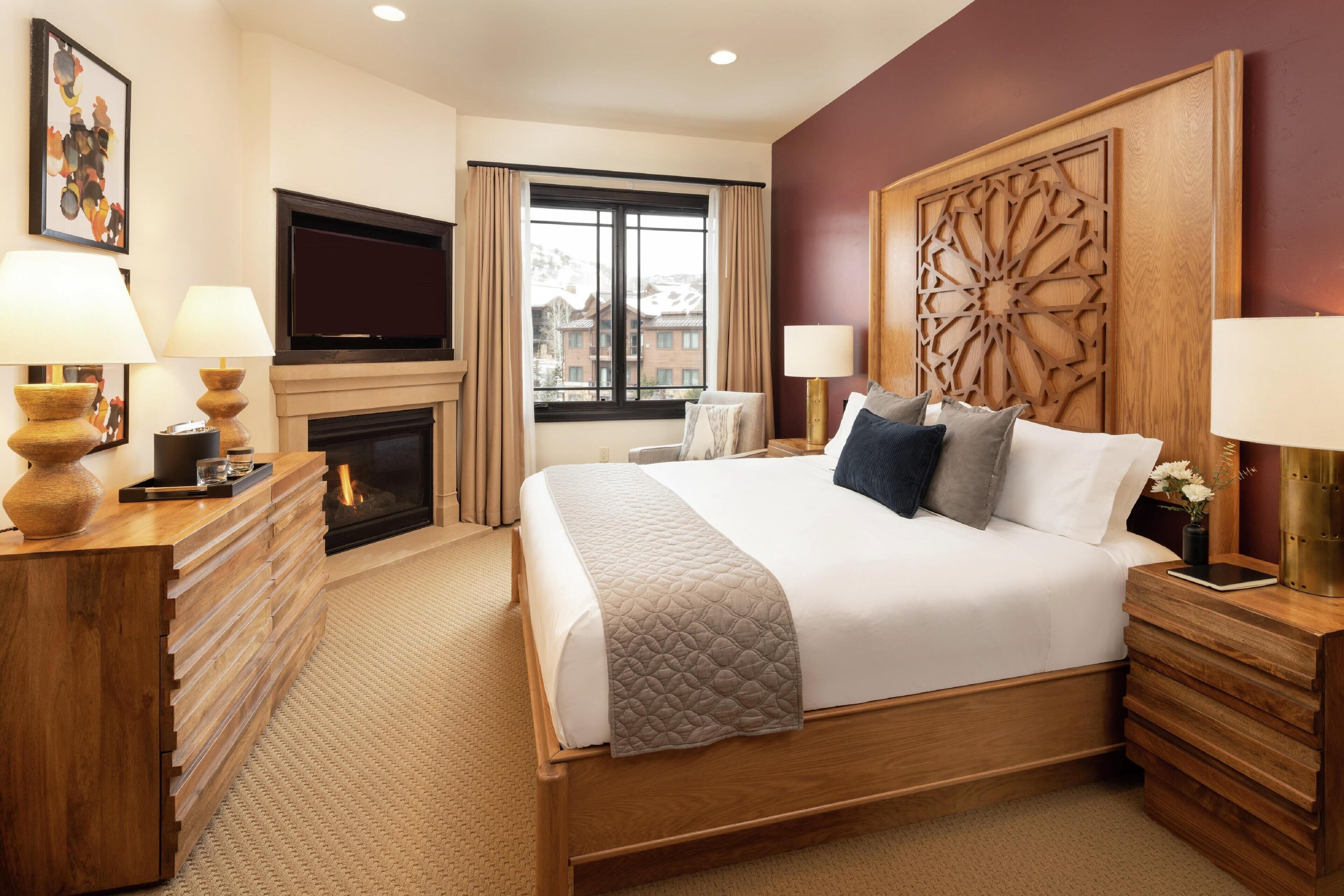 A hotel room with a large bed, wooden headboard, a fireplace, a TV, and a view of the outside.