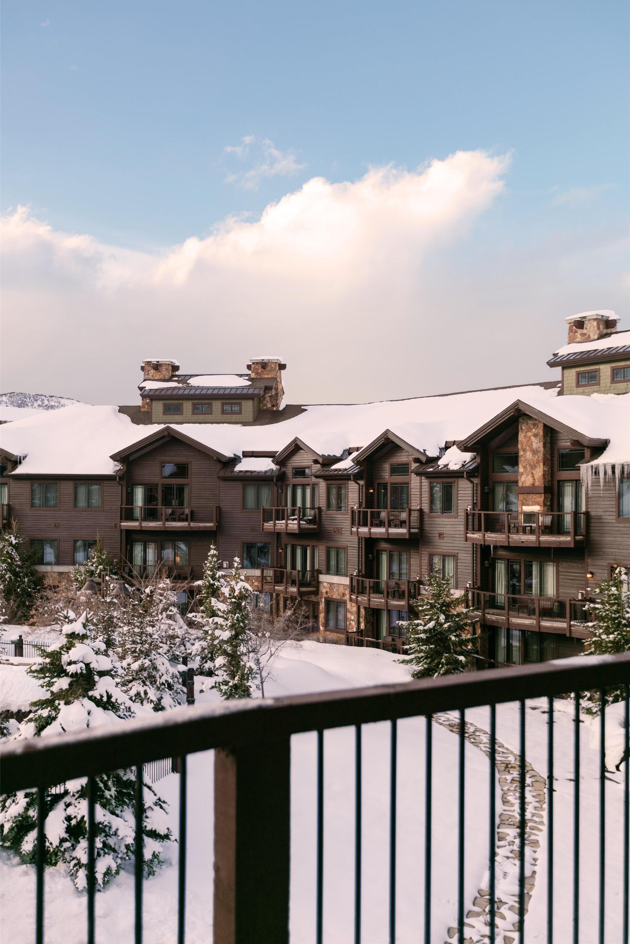 A multi-story lodge with wooden exterior and balconies, surrounded by snow-covered trees and mountains.