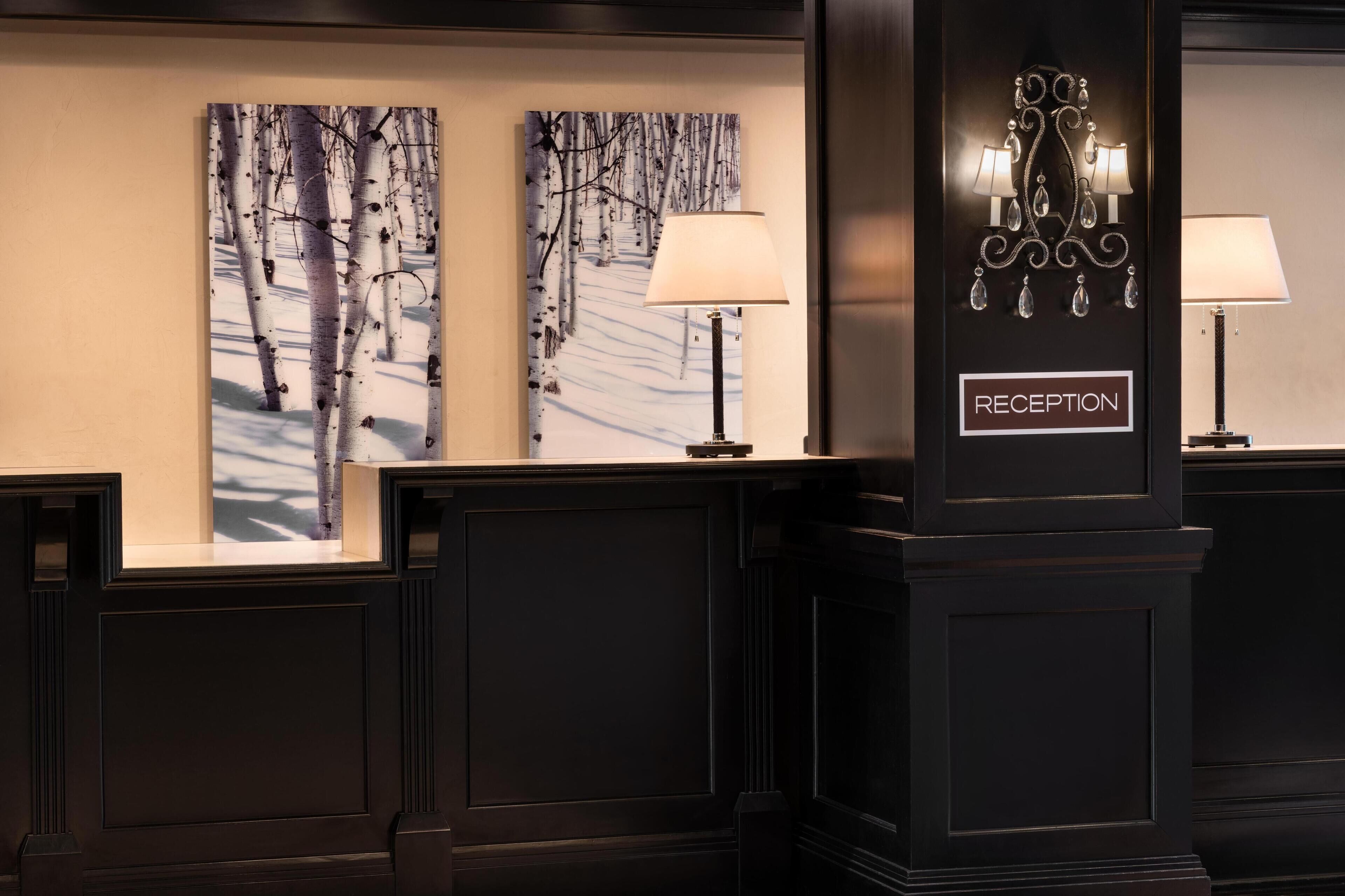 A reception area with two wall-mounted lamps, a 'RECEPTION' sign, and two framed winter forest paintings.
